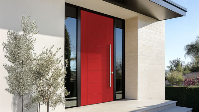 A striking modern front door in a vibrant Habanero Chile red finish makes a bold statement against a minimalist, neutral-toned exterior. Featuring a sleek horizontal panel design and an elongated vertical pull handle, the door is framed by narrow sidelites that allow natural light to enhance the entryway. A clean stone entry step and surrounding landscaping complete the contemporary look.