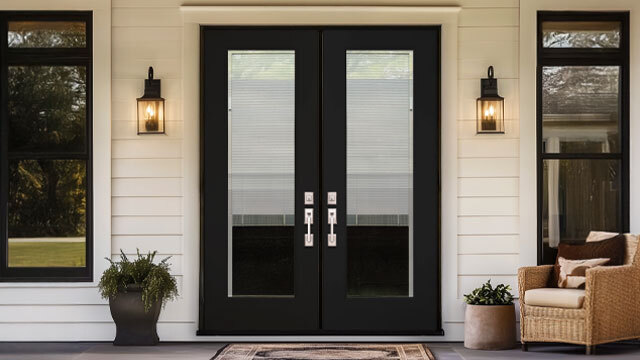 A stylish set of modern double patio doors in a matte black finish, featuring full-view glass panels with built-in blinds for added privacy and light control. Framed by a white exterior with black-trimmed windows and classic lantern sconces, the setup exudes contemporary farmhouse charm. Comfortable outdoor seating and potted plants complete the welcoming porch scene.